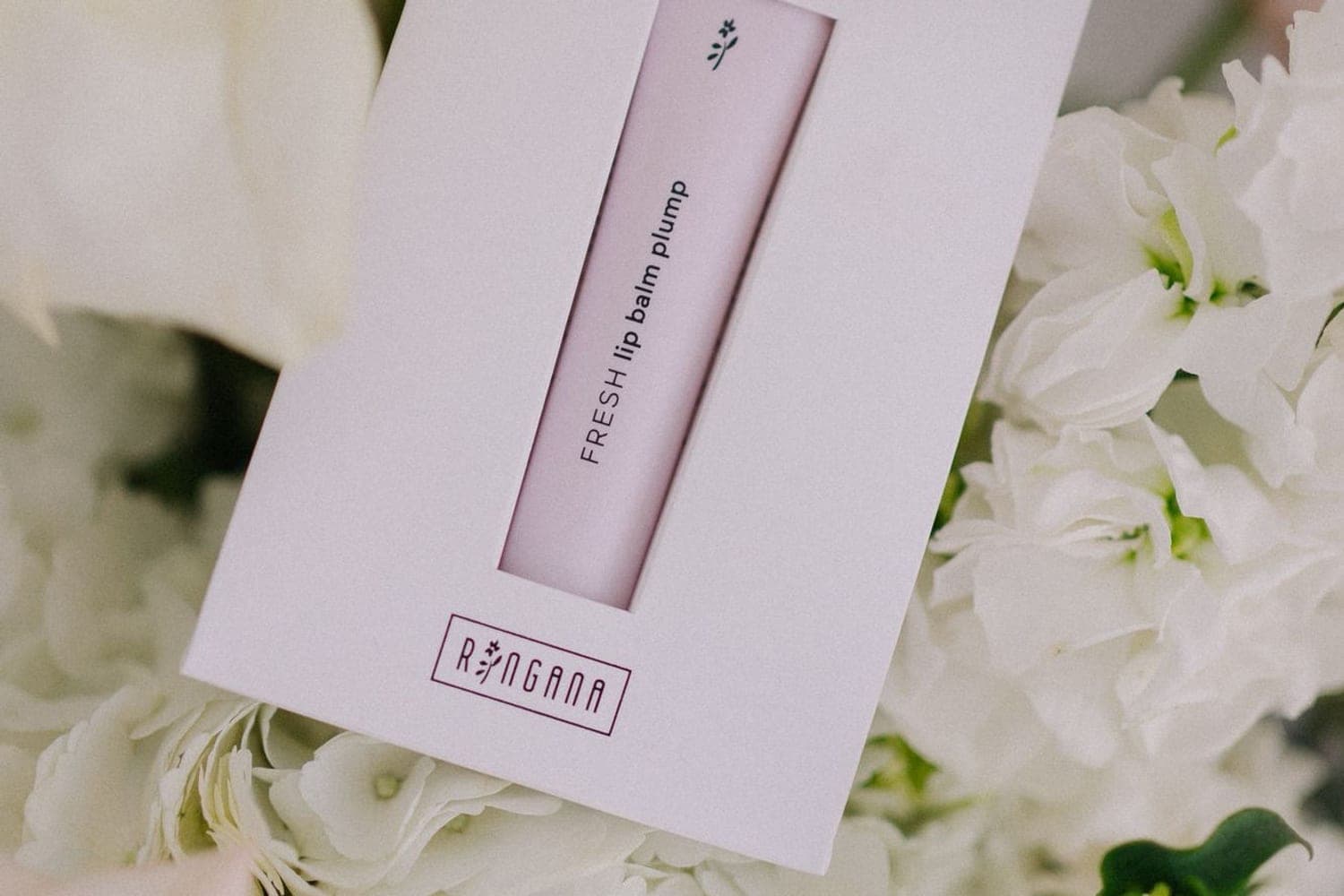 RINGANA FRESH lip balm plump in der Verpackung zwischen weissen Blueten
