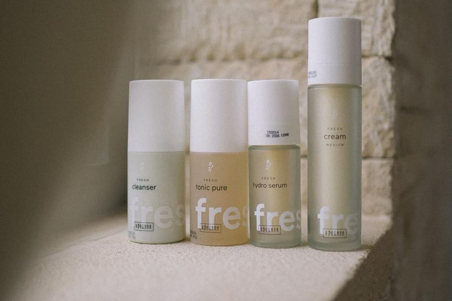 RINGANA FRESH cleanser, tonic pure, hydro serum und cream im Sonnenlicht auf einer Steinmauer